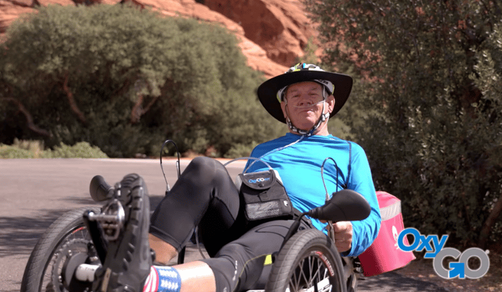 Older male on oxygen riding a three wheeled road bike.